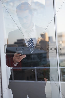 Businessman sending a text seen through window