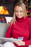 Festive blonde woman using her credit card and tablet pc