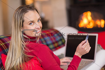 Smiling blonde shopping online with laptop at christmas