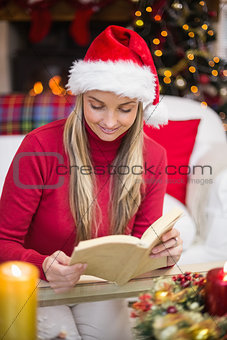 Pretty blonde in santa hat reading book at christmas time