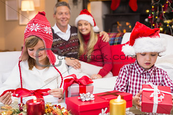 Festive little siblings opening a gift in front of their parents