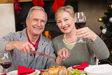 Man carving chicken while his wife drinking red wine