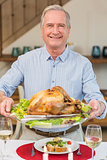 Happy mature man holding roast turkey at christmas dinner