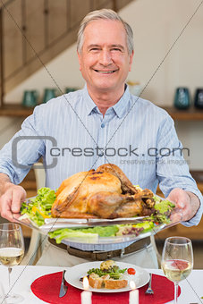 Happy mature man holding roast turkey at christmas dinner