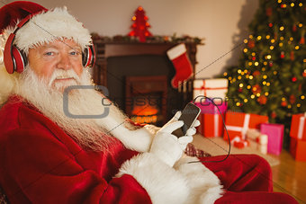 Smiling santa listening music with his smartphone