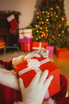 Santa claus holding a red gift with a white bow