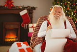 Smiling santa writing list on the armchair