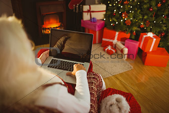 Santa sitting on the armchair and typing on laptop