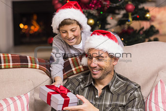 Son offering father a christmas gift on the couch
