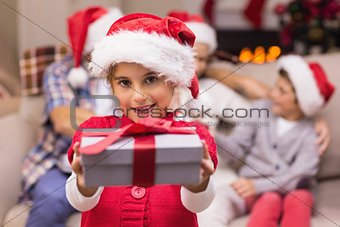 Smiling little girl offering a gift with her parents behind