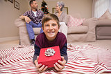 Happy son lying and holding gift with his family behind