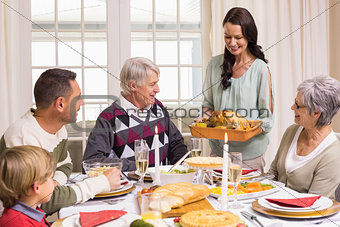 Woman holding turkey roast with family at dining table