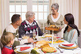 Grandmother holding turkey roast with family at dining table