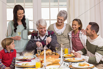 Grandfather carving chicken and his family looking him