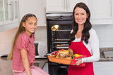 Happy mother and daughter posing with roast turkey