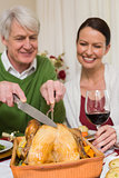 Grandfather carving chicken while woman drinking red wine