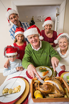 Grandfather in santa hat carving chicken at christmas dinner