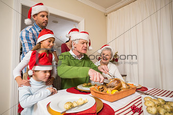 Grandfather in santa hat carving chicken at christmas