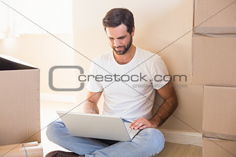 Happy man using laptop surrounded by boxes