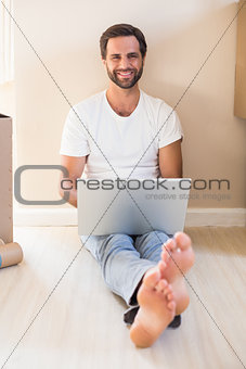 Happy man using laptop surrounded by boxes