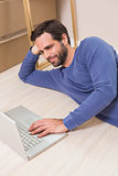 Happy man lying on floor using laptop