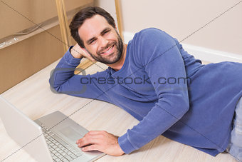 Happy man lying on floor using laptop