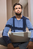 Depressed man sitting on floor using laptop