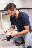 Plumber crouching and taking notes