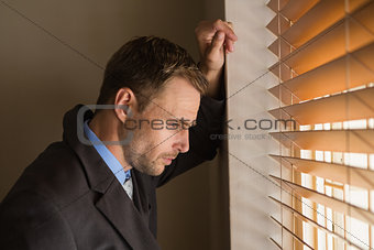 Serious businessman peeking through blinds