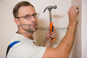 Handyman hammering nail in wall while looking at camera