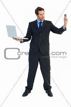 Businessman using laptop and texting on smartphone