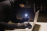 Robber hacking a laptop while making light with his phone