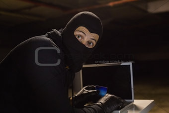 Burglar shopping online with laptop while looking at camera