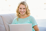 Portrait of smiling blonde sitting on couch using laptop