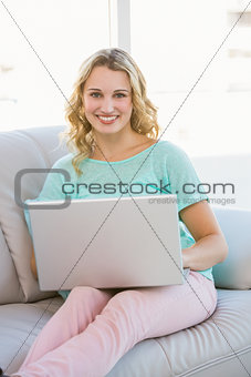 Smiling casual blonde sitting on couch using laptop