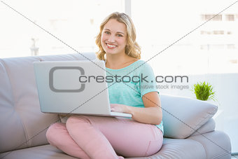 Happy casual blonde relaxing on couch using laptop