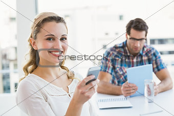 Woman sending a text message with her colleague behind