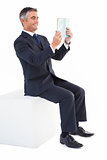 Smiling businessman sitting on a cube reading a book