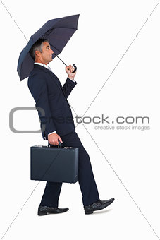 Businessman walking and holding briefcase under umbrella