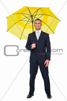 Smiling businessman under yellow umbrella
