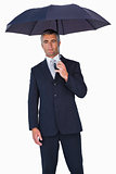 Cheerful businessman in suit under umbrella