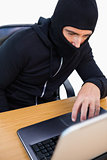 Thief with balaclava hacking a laptop