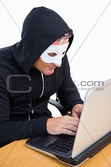 Burglar with white mask hacking a laptop