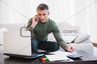 Man with laptop phoning and taking notes