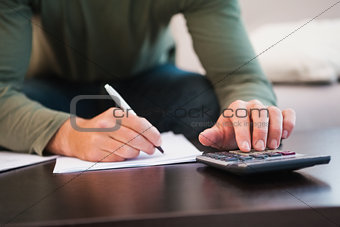 Mid section of man taking notes and using calculator