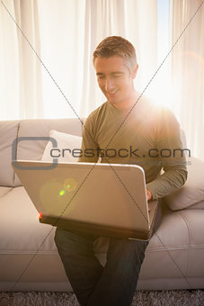 Smiling man sitting on couch using laptop