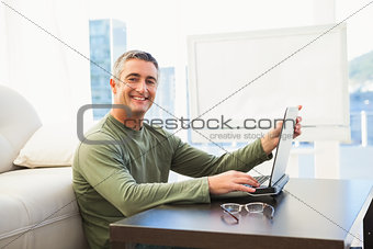 Smiling man using laptop with glasses on the table