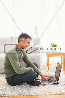 Smiling man sitting on carpet using laptop