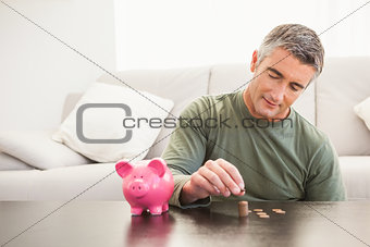 Smiling man putting some coins into a piggy bank
