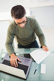 Man with glasses reading paper and using laptop